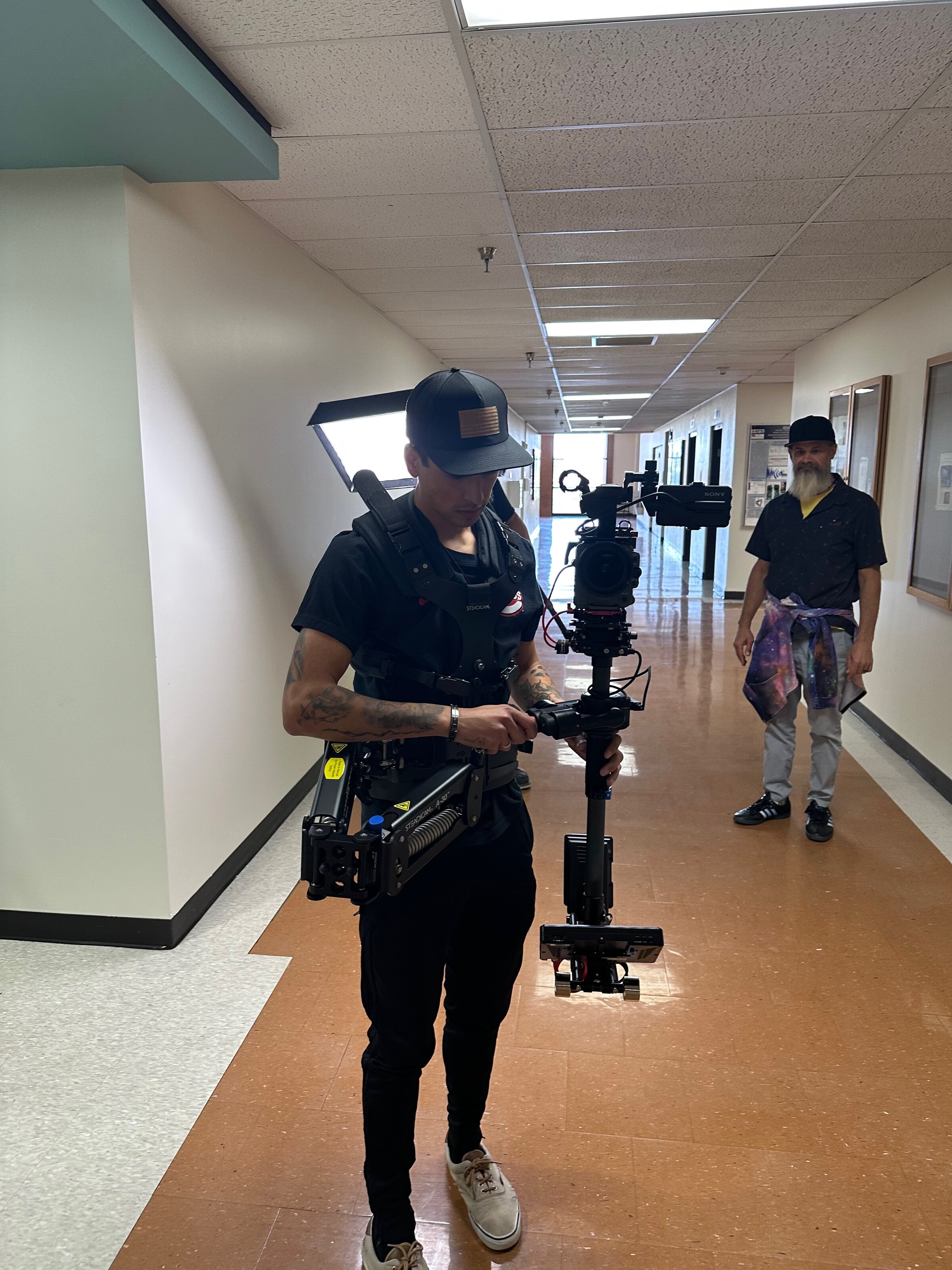 A camera operator works with a stabilized rig on location in a hallway.